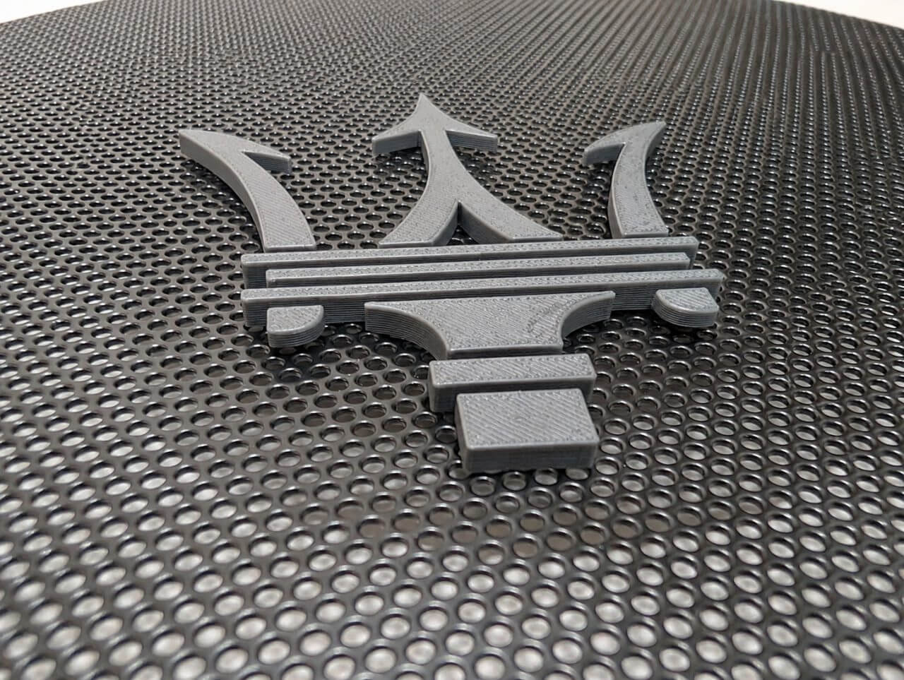 Black 3D-printed Maserati emblem mounted on perforated metal