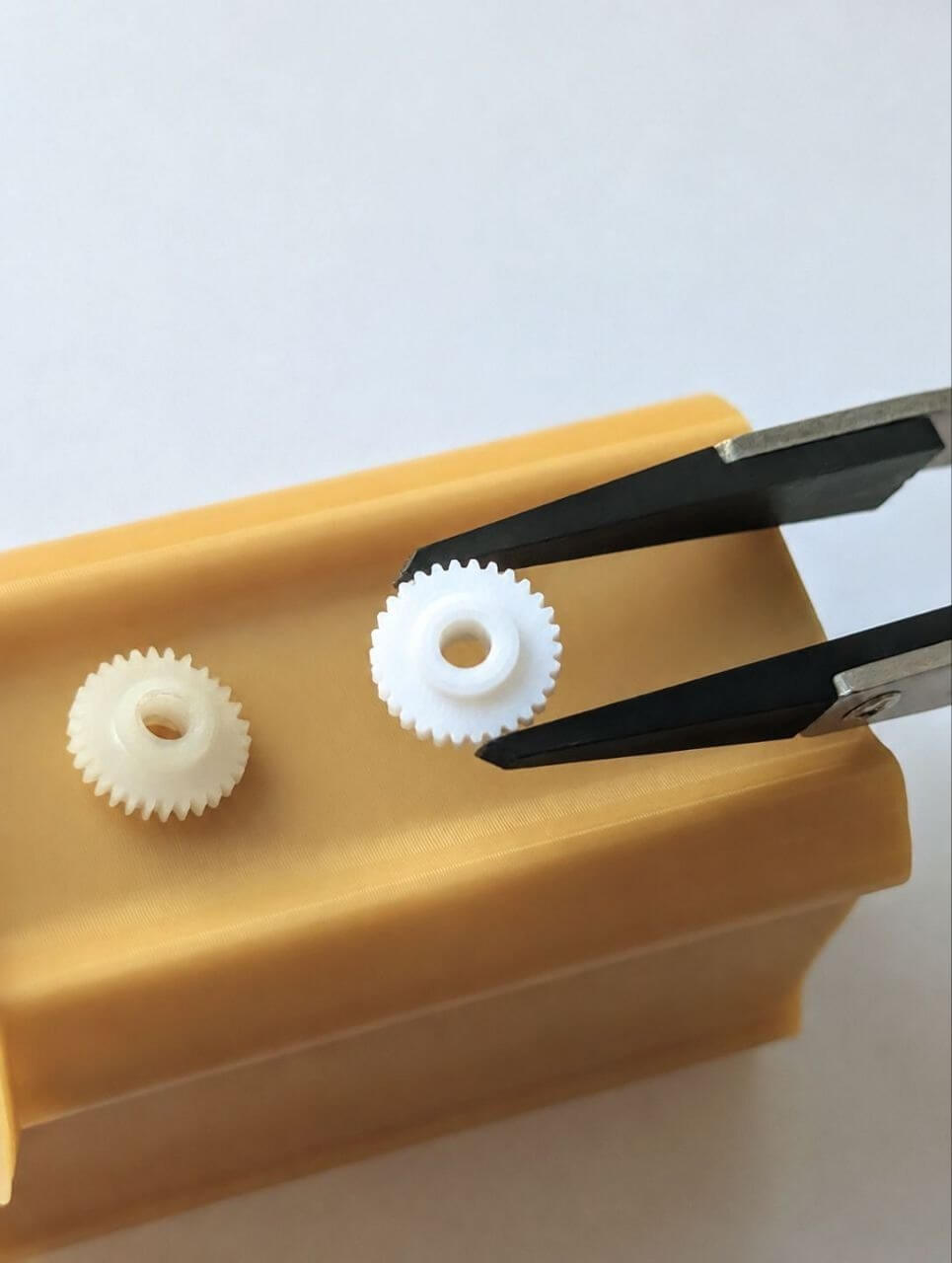 Small 3D-printed gear held with tweezers beside a larger gear