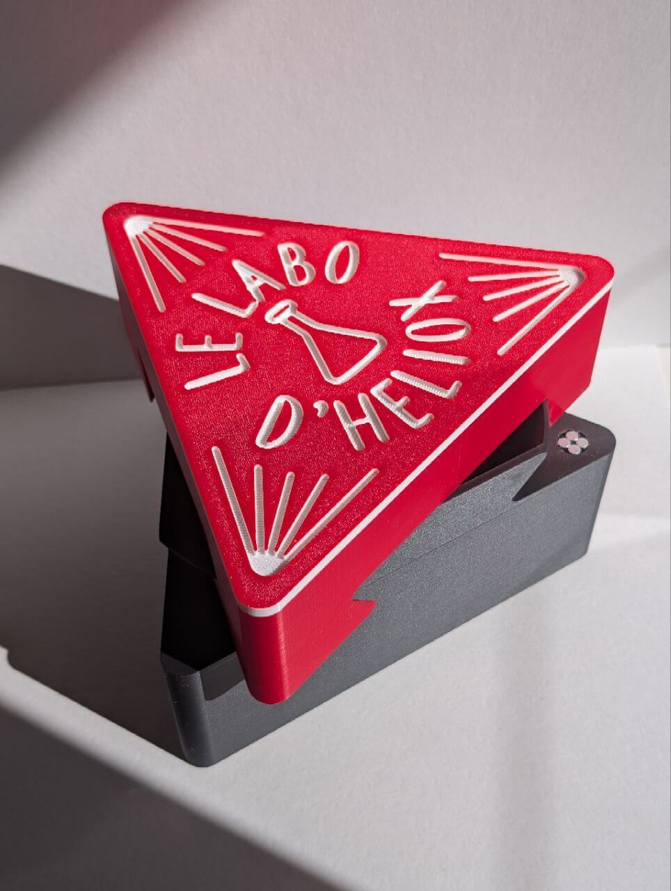 Red triangular box with engraved logo and text on a gray stand