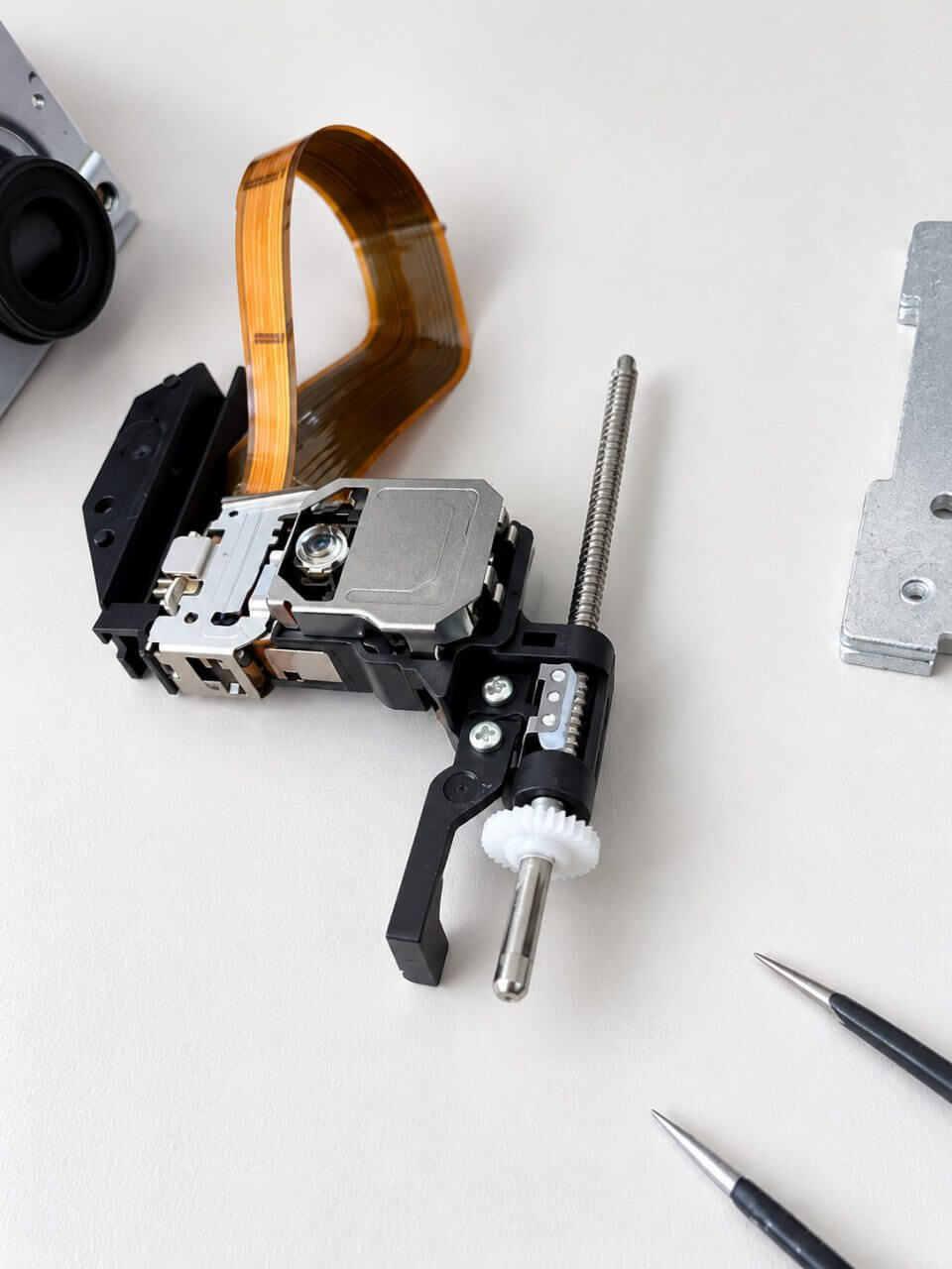 Disassembled laser mechanism with a gear and ribbon cable
