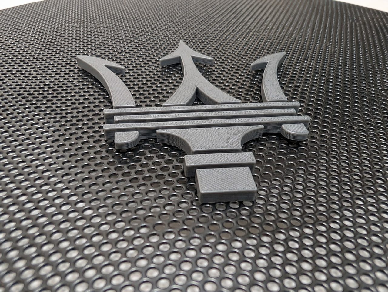 Black 3D-printed Maserati emblem mounted on perforated metal