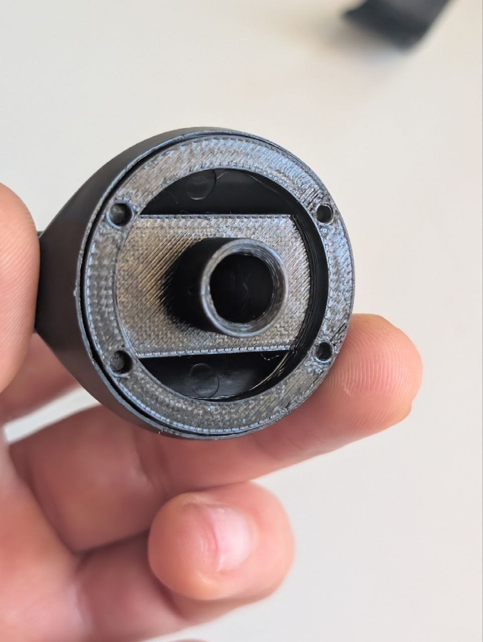 Black cylindrical cover held in hand with four mounting holes