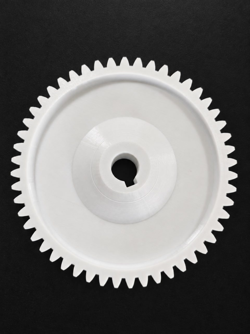 White 3D-printed gear photographed on a black background